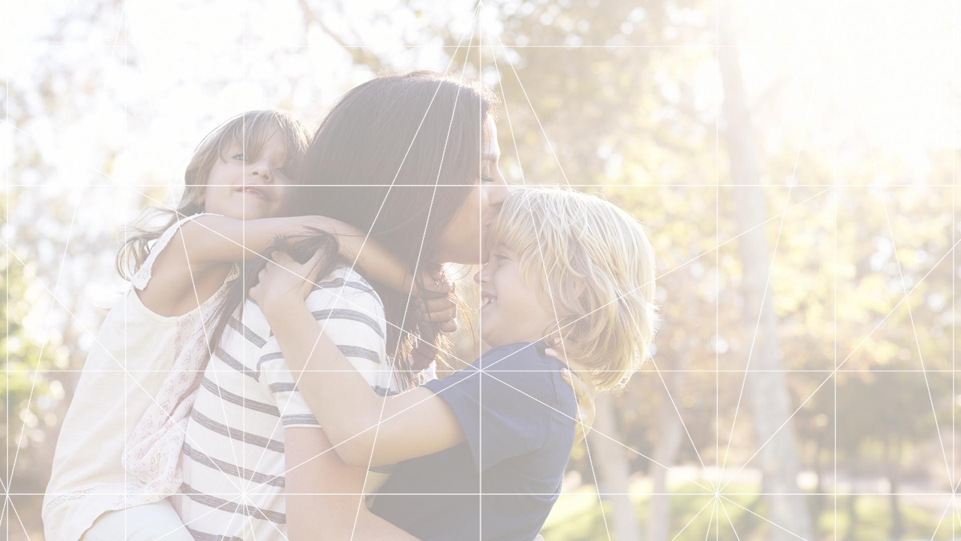 A mother giving a piggyback ride to a small child while kissing another child on the forehead