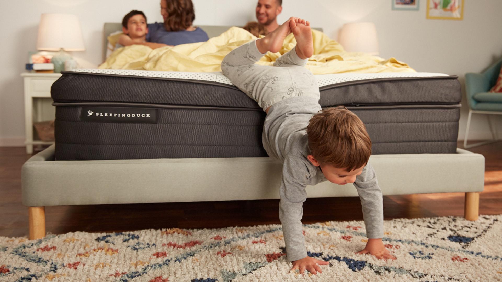 A pregnant woman and a man in a SD Mach 2 bed with their three kids, one playing near the foot of the bed and falling off.