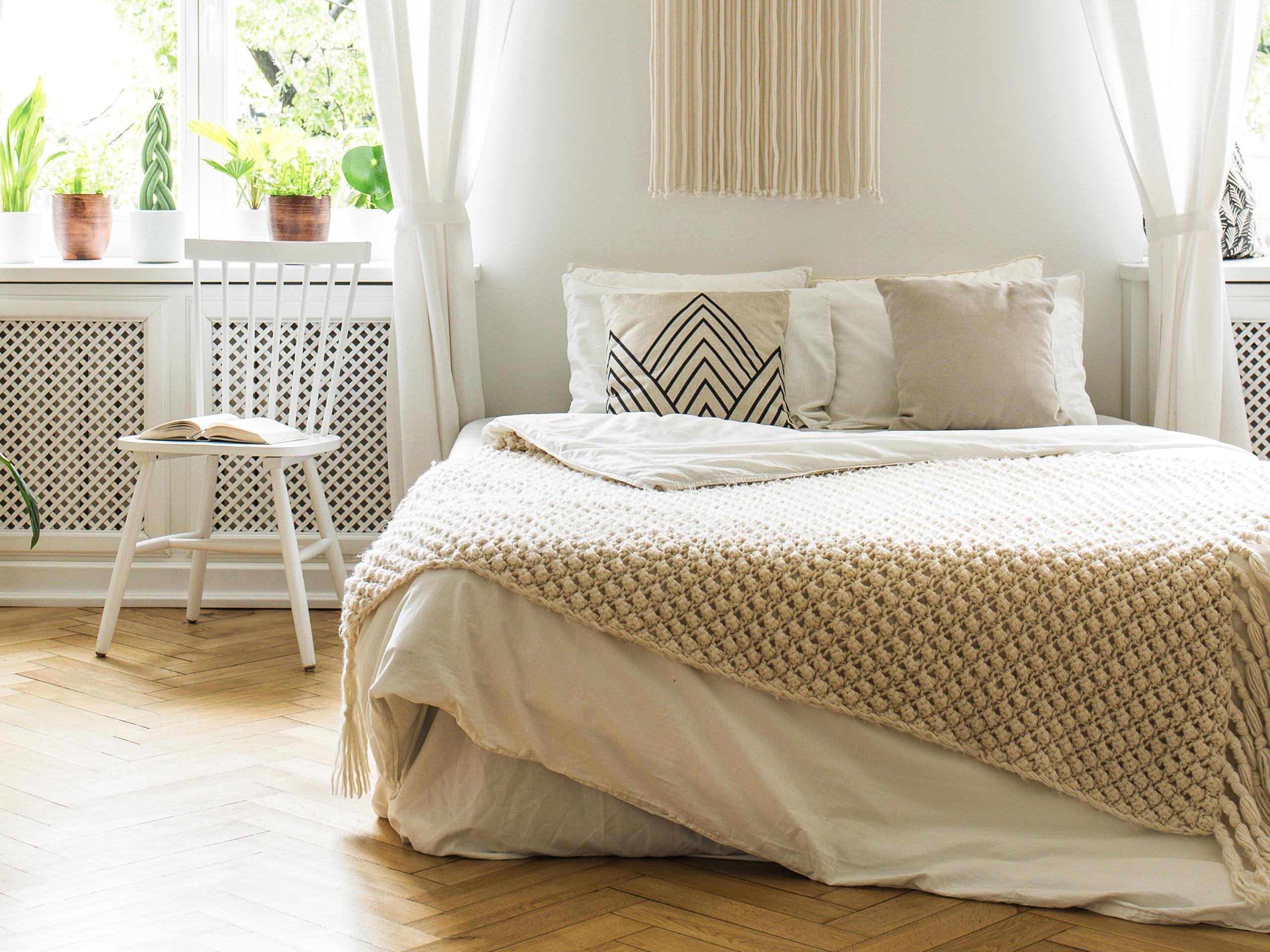 A bed in the centre of a light-filled and neutral tone bedroom, with plants on the windowsill.