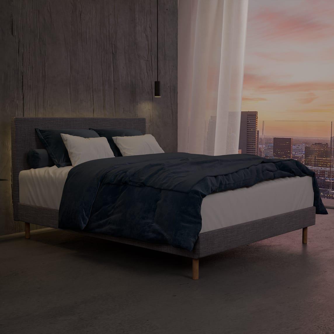 The Boyd SD Indestruct Bed in Charcoal, in an industrial bedroom overlooking a morning city skyline.