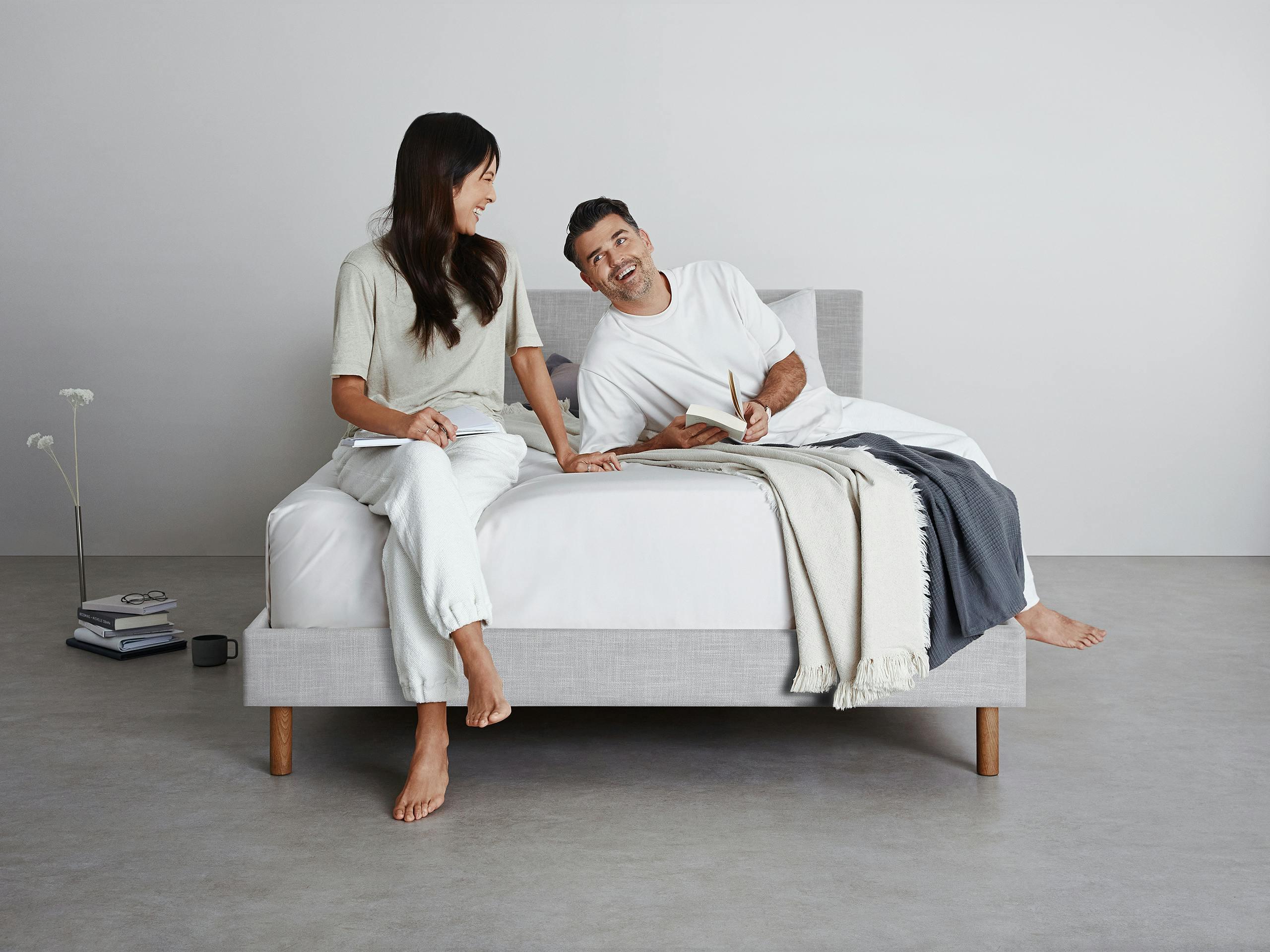 A couple, sitting on a light grey SD Indestruct Bed bed frame and mattress.